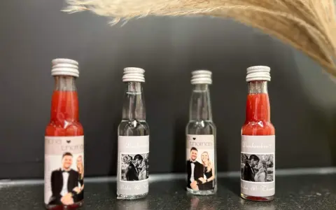 Vier kleine Flaschen mit personalisierten Etiketten, die Hochzeitsfotos und Namen zeigen. Perfekt als Schnaps zum selber machen für Gäste.
