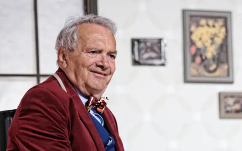 Uśmiechnięty Zdzisław Wardejn, znany z wielu filmów, w bordowym marynarkowym stroju i kolorowym krawacie.