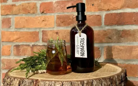 Zutaten für Rosmarinwasser Haare selber machen: frischer Rosmarin, ein Glas mit Flüssigkeit und eine dunkle Flasche mit Pumpspender.