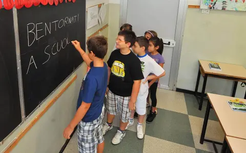 Schulkinder stehen vor einer Tafel mit der Aufschrift "Bentornati a scuola". Sie warten gespannt, wie viele Schultage ein Jahr hat.