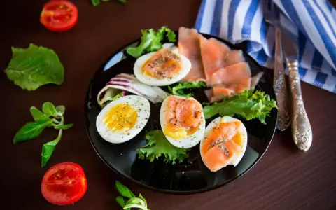 Jajka na twardo z łososiem i sałatą, idealne na dietę low carb. Pomidorki i zioła dopełniają danie.