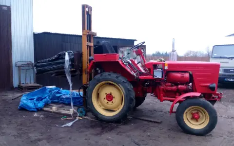 Czerwony traktor z ładowarką czołową, gotowy do pracy. Może posłużyć do budowy masztu do ciągnika.