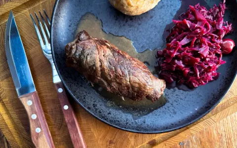 Herzhafte Rouladen im Dutch Oven zubereitet, serviert mit Rotkohl und Klößen auf einem rustikalen Teller.