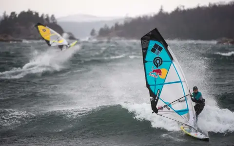 Windsurferzy na falach, jeden z nich na pierwszym planie, w akcji.