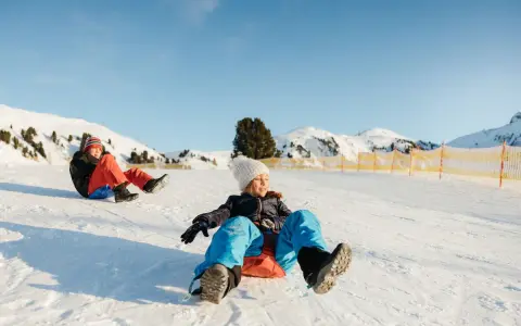 Bambini felici scendono con slittino su pendio innevato. L'altitudine neonati non è un problema per queste avventure invernali.