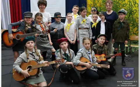 Dzieci w strojach harcerskich grają na gitarach i mandolinie. To może być zapowiedź piosenki o harnasiu.