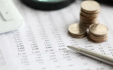 Monedas apiladas sobre un informe financiero, con una calculadora y un bolígrafo. El informe muestra números, quizás el modelo 420.