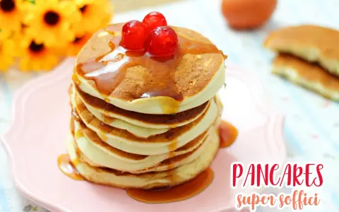 Pancakes con albumi, soffici e dorati, guarniti con sciroppo e ciliegie rosse, su un piatto rosa.