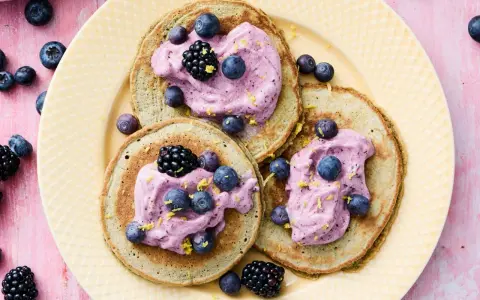 Tre fluffiga pannkakor med havregryn toppas med lila grädde, blåbär och björnbär. Strössel av citronskal ger en frisk touch.