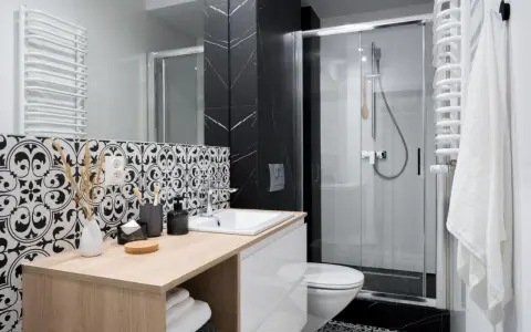 Élégante petite salle de bain italienne avec carrelage noir et blanc, douche moderne et meuble vasque en bois clair.