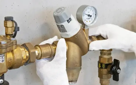 Mani guantate installano un riduttore di pressione acqua, mostrando come funziona con manometro.