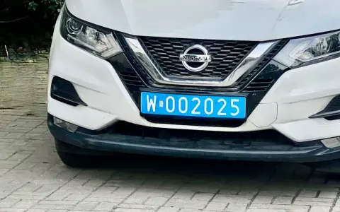 Biały Nissan z niebieską tablicą rejestracyjną W-002025, wskazującą na dyplomatyczne tablice rejestracyjne.