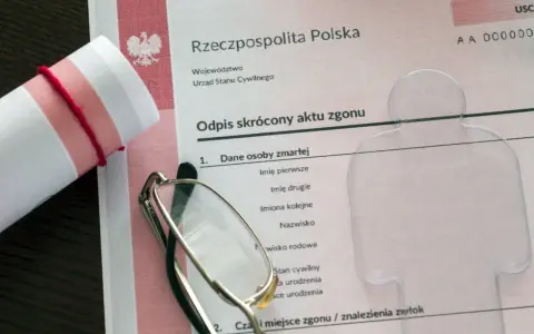 Zrolnowany dokument z orłem, okulary i formularz "Odpis skrócony aktu zgonu".