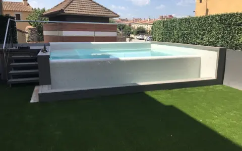 Moderna piscina con mosaico blanco, rodeada de césped artificial y setos. Ideal para decoración de terrazas con piscina.