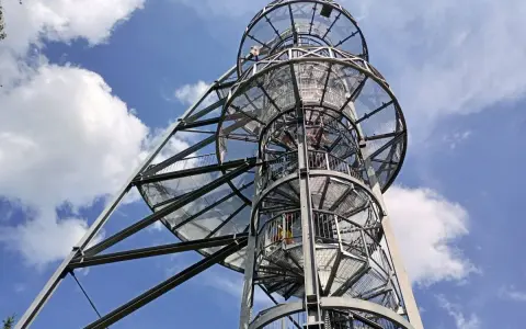 Metalowa wieża widokowa na Młynicy z krętymi schodami pnącymi się ku niebu. Widać ludzi wspinających się na szczyt.