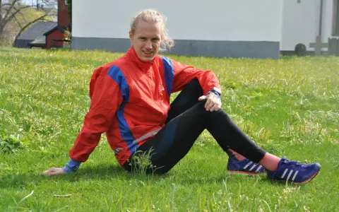 En löpare i röd jacka och svarta tights vilar i gräset, redo att springa milen under 50 minuter.