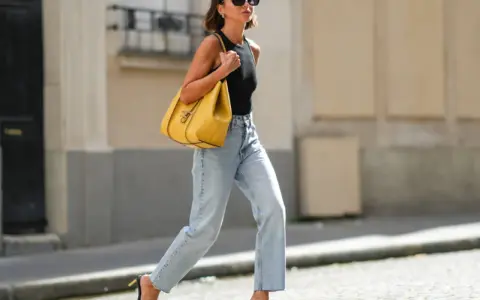 Mujer con vaqueros anchos de tiro alto, un top negro y un bolso amarillo vibrante. Un ejemplo de los diversos tipos de vaqueros mujer.