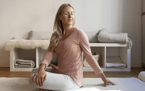 Kvinna i rosa tröja och grå byxor gör en vridning i sittande ställning, en form av gående meditation.