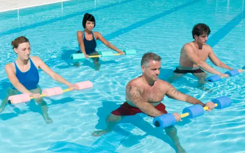 Quatre personnes font un exercice piscine avec des haltères flottants. L'eau bleue reflète la lumière du soleil.