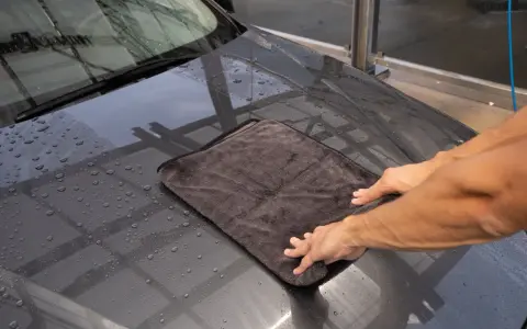 Hände trocknen das nasse Auto mit einem weichen auto trockentuch.