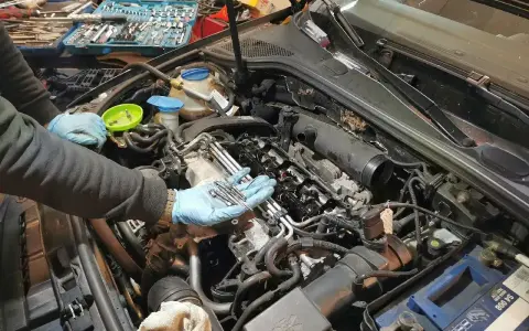 Mechanik w niebieskich rękawiczkach trzyma nowe świece żarowe, przygotowując się do ich wymiany w silniku samochodu.
