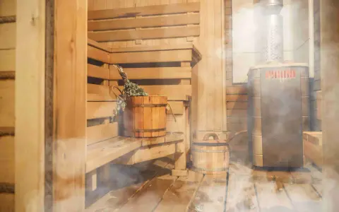 Drewniana sauna z piecem, ławami i wiaderkiem z miotełką. Idealne miejsce, by dowiedzieć się, jak zbudować saunę i odpocząć.