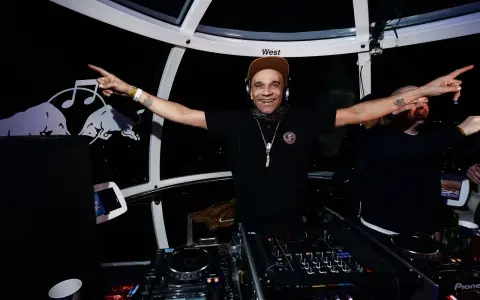 Un dj rap souriant, casqué, bras écartés, anime la soirée dans une cabine panoramique.