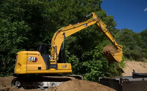 Żółta koparka Cat 313 z łyżką pełną ziemi, gotowa do pracy. Dane techniczne tej maszyny budowlanej są imponujące.