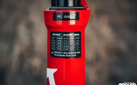 Czerwiony amortyzator Rock Shox z naklejką zawierającą tabelę ciśnień i ustawień powrotu dla różnych wag rowerzysty.