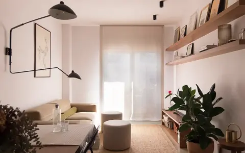 Salón moderno con sofá beige, mesa y dos pufs. Las paredes lucen un impecable **microcemento acabado**, aportando elegancia y minimalismo.