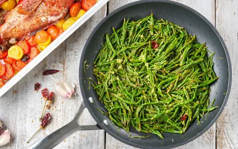 Asparagi di mare saltati in padella con aglio e peperoncino, accanto a un pesce al forno con pomodorini.