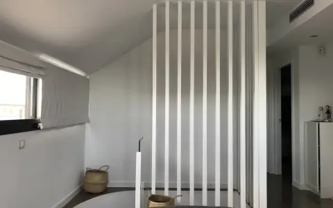 Modern interior with a white slatted partition, possibly to tirar tabique para unir dos pisos. Baskets and a window are visible.