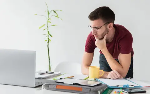 Joven autónomo reflexiona en su escritorio. Lo cotizado como autónomo cuenta para el paro, una tranquilidad para su futuro.
