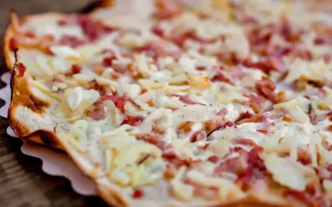 Tarte flambée gourmande, spécialité d'un restaurant alsacien à Nantes. Crème, lardons et oignons sur une pâte fine et croustillante.