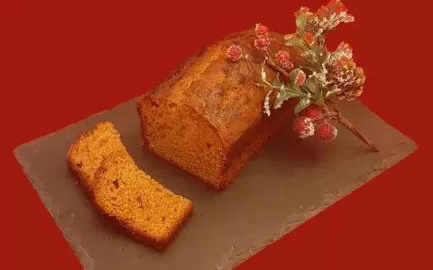Un délicieux pain d'épice, décoré de baies rouges et de branches givrées, est prêt à être dégusté. Une tranche est déjà coupée.