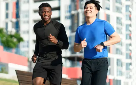 Deux hommes souriants courent ensemble dans un parc, profitant de leur routine pour courir tous les jours.