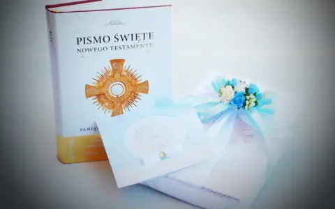 Dedykacja na komunię: Pismo Święte, ozdobna kartka i prezent z błękitną wstążką i kwiatami.