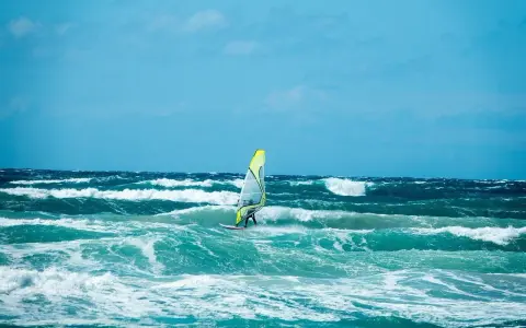 Windsurfer na wzburzonym, turkusowym morzu pod błękitnym niebem.