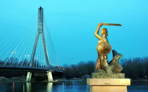 Warszawska Syrenka, bohaterka legendy, stoi dumnie z mieczem i tarczą. W tle widać nowoczesny most.