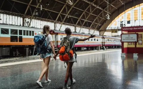 Dwie podróżniczki z plecakami idą wzdłuż peronu, gdzie stoi długi pociąg. Może to być ich pierwszy pociąg Eurostar.