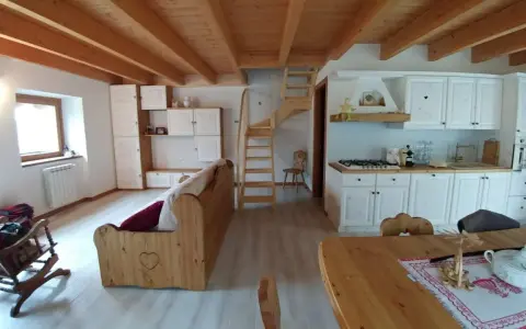 Come arredare una taverna: cucina bianca, divano in legno, scala a vista e soffitto a travi.