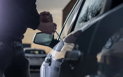 Tentativo di furto d'auto: un uomo usa un cacciavite per forzare la portiera, un'azione che rientra nella verifica veicoli rubati.