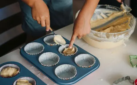 Dziecko nakłada ciasto na muffinki łyżką do formy.