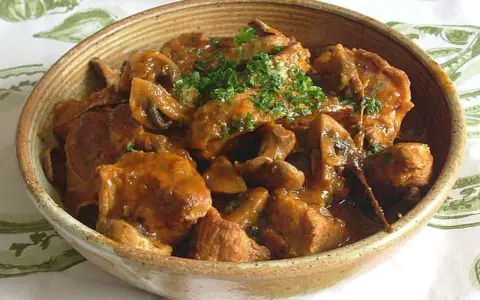 Un délicieux sauté de veau aux champignons, garni de persil frais, servi dans un bol en terre cuite.