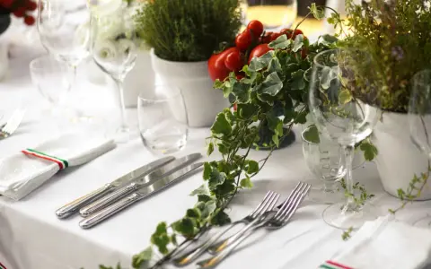 Elegancko nakryty stół na wesele, z kieliszkami, sztućcami i ozdobami z pomidorków i bluszczu. Idealne miejsce na wino na wesele.