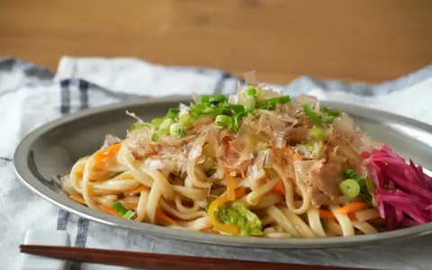 Makaron udon z warzywami, posypany szczypiorkiem i płatkami bonito, na talerzu.