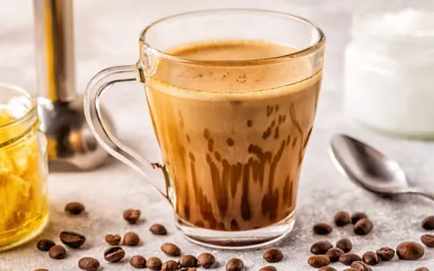 Kawa bullet coffee w szklance, obok ziarna kawy, słoiczek z miodem i łyżeczka.