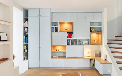 Aménagement d'un **pièce à vivre** moderne avec bibliothèques modulables, rangements intégrés et un banc cosy près de l'escalier.