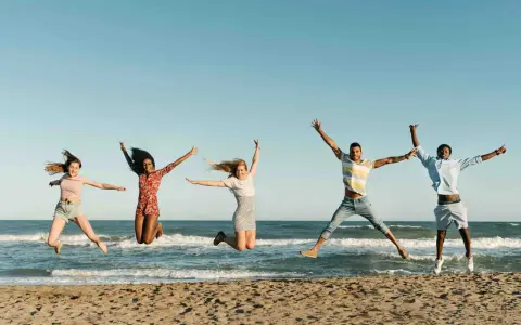 Fünf junge Leute springen ausgelassen am Strand. Sie freuen sich über ihr Sprachreise Stipendium und die Freiheit.