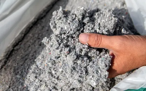 Gros plan sur une main tenant un tas de fibre de cellulose isolant, un matériau gris et vaporeux.
